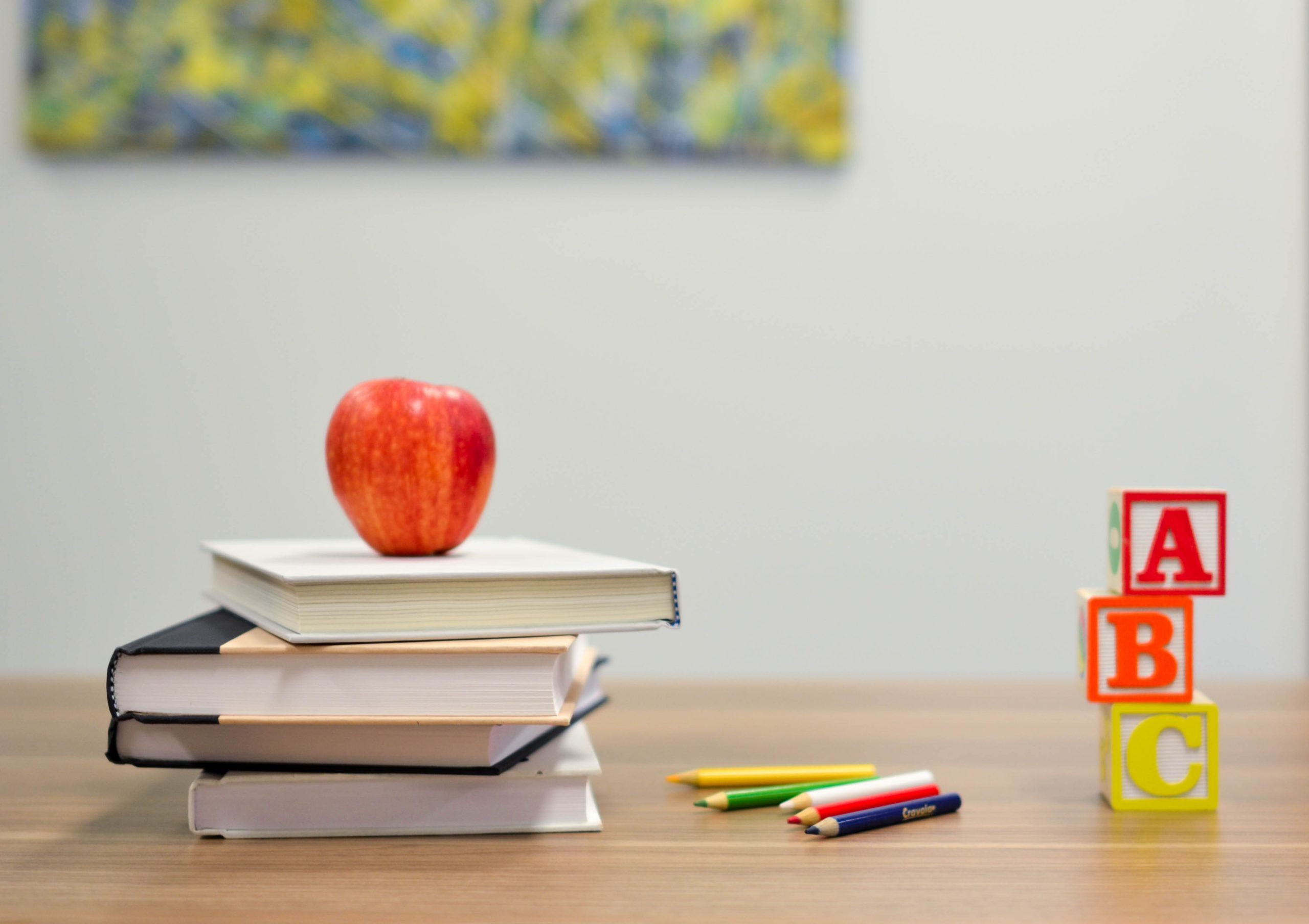 An apple on a pile of books and some ABC blocks on a desk