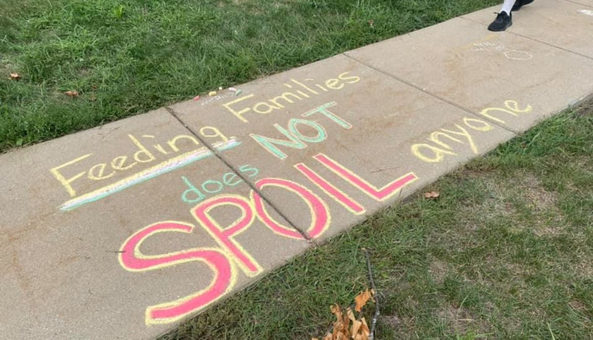 Red, yellow, and green chalk on a sidewalk that says "Feeding families does not SPOIL anyone"