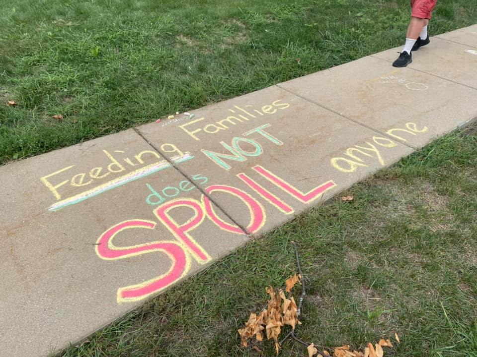 Red, yellow, and green chalk on a sidewalk that says "Feeding families does not SPOIL anyone"