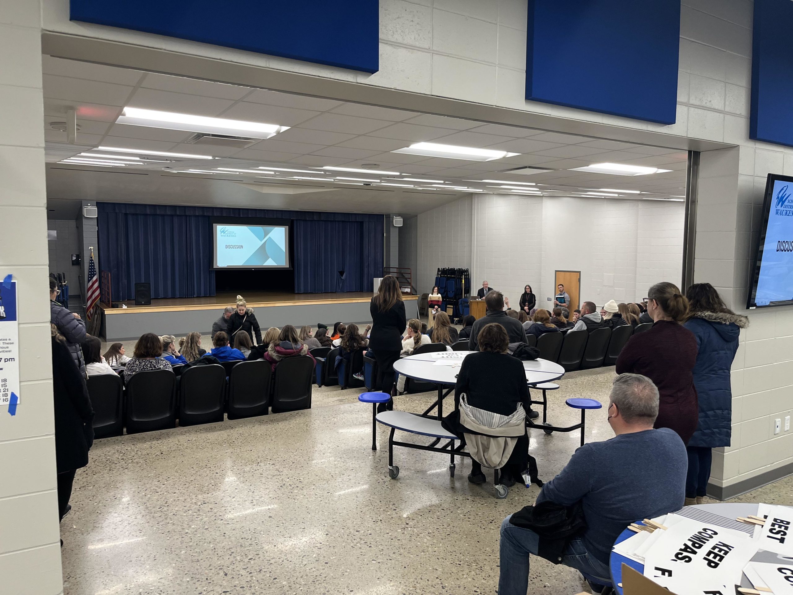 View looking in to the Butler Middle School auditorium, where the seats are full and there are people standing behind.